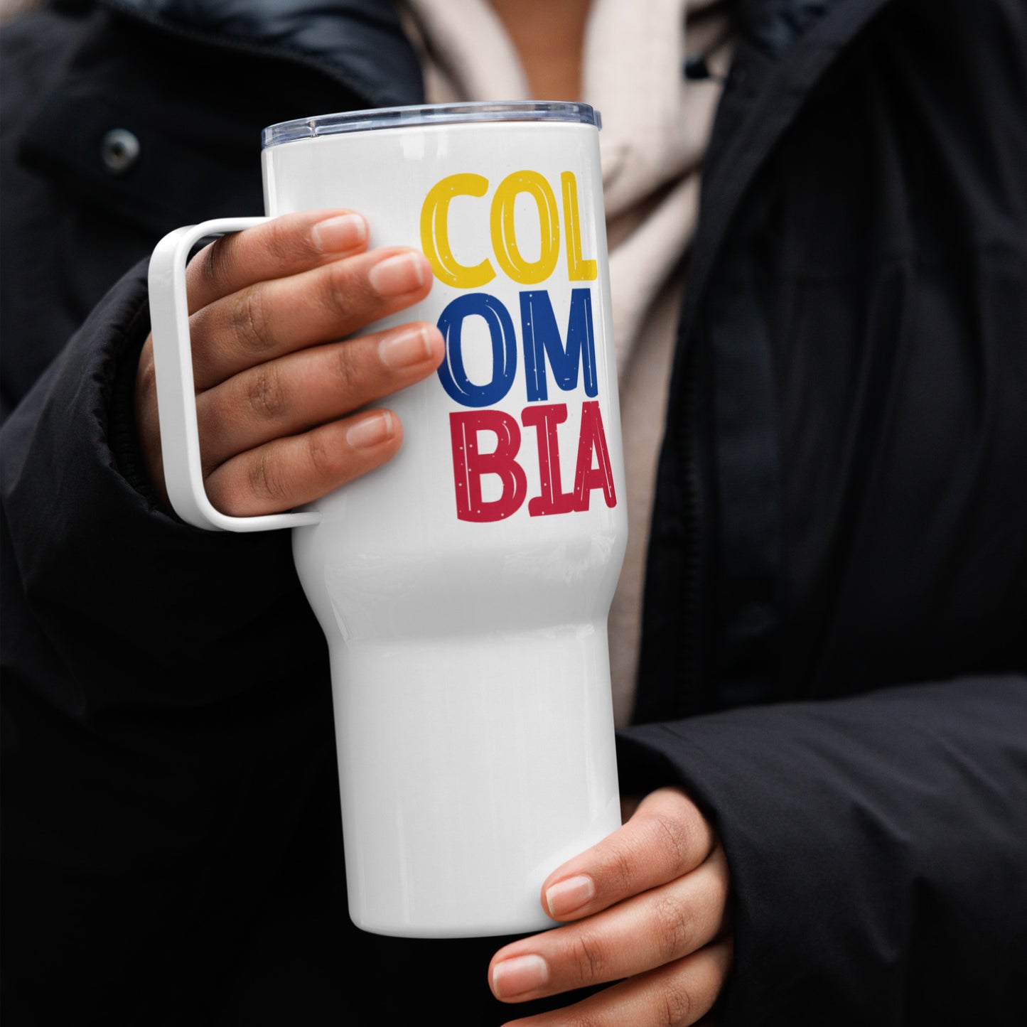 White 25oz travel mug with a sturdy handle, featuring 'Colombia' printed in bold yellow, blue, and red letters. Designed for hot and cold drinks, perfect for on-the-go use.